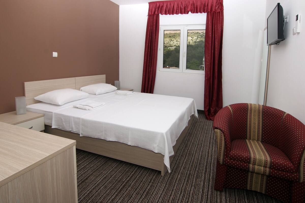 A hotel room with a bed, a desk, a chair, and a TV.