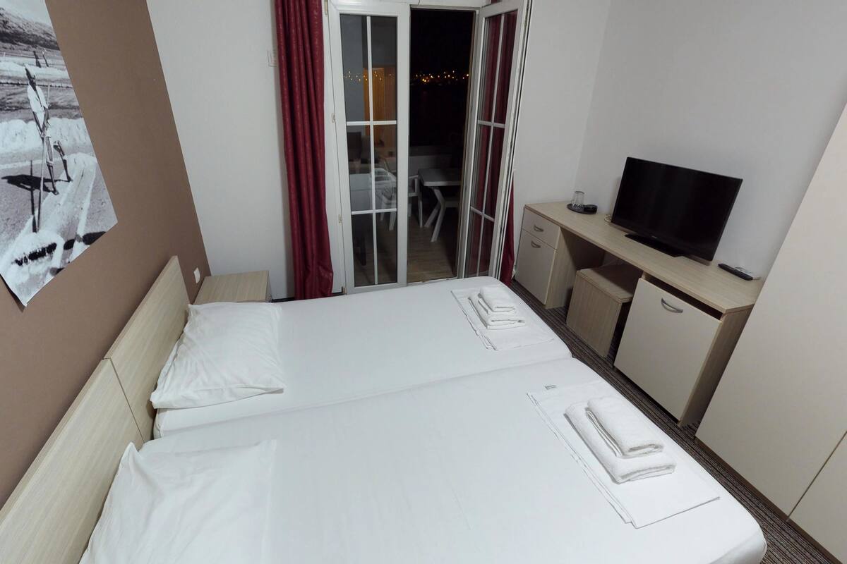 A hotel room with a bed, a desk with a television, and a sliding door leading to a balcony.