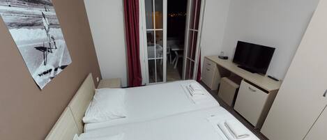 A hotel room with a bed, a desk with a television, and a sliding door leading to a balcony.