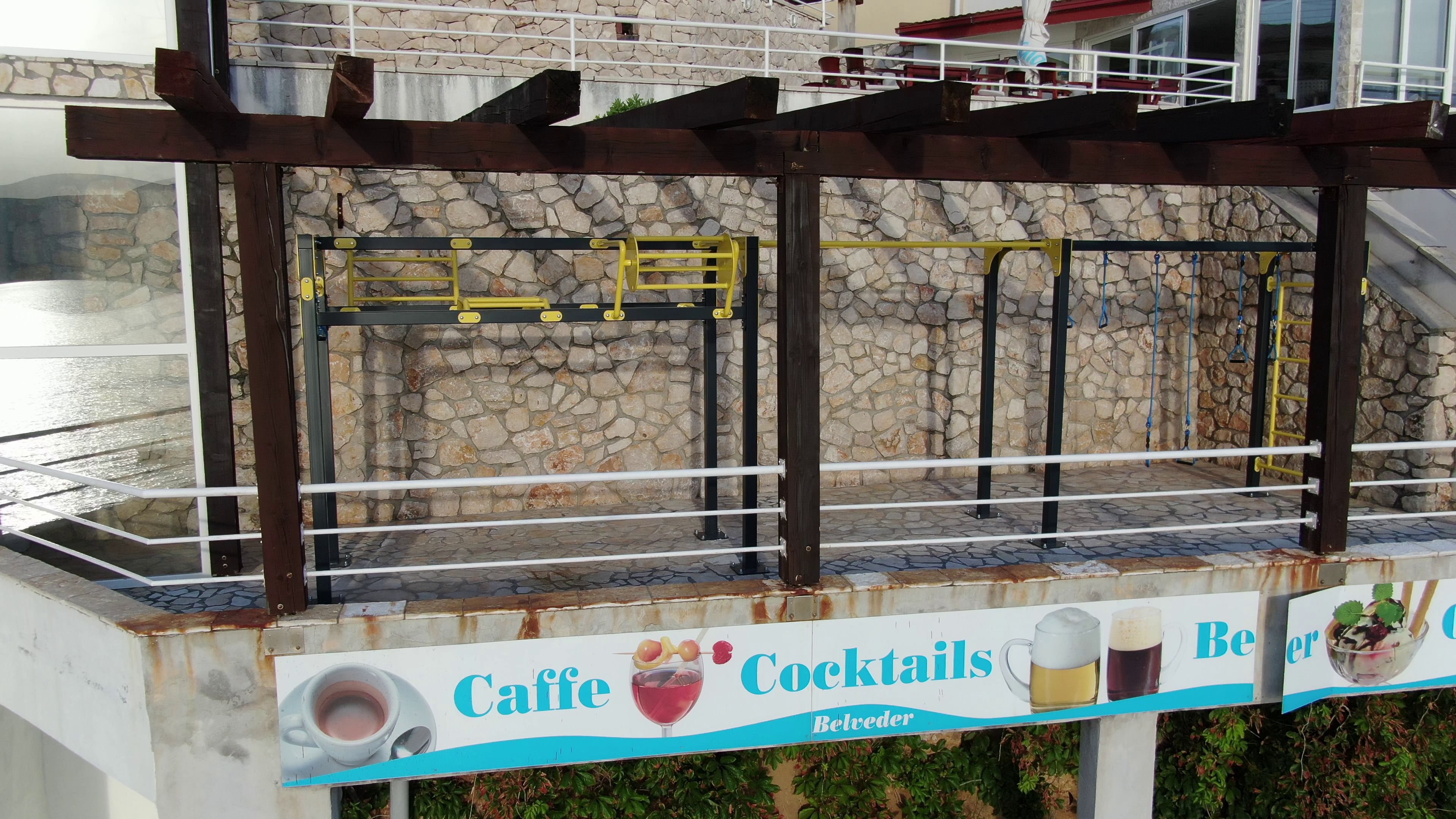 A stone wall with a metal railing and a sign advertising caffe cocktails.