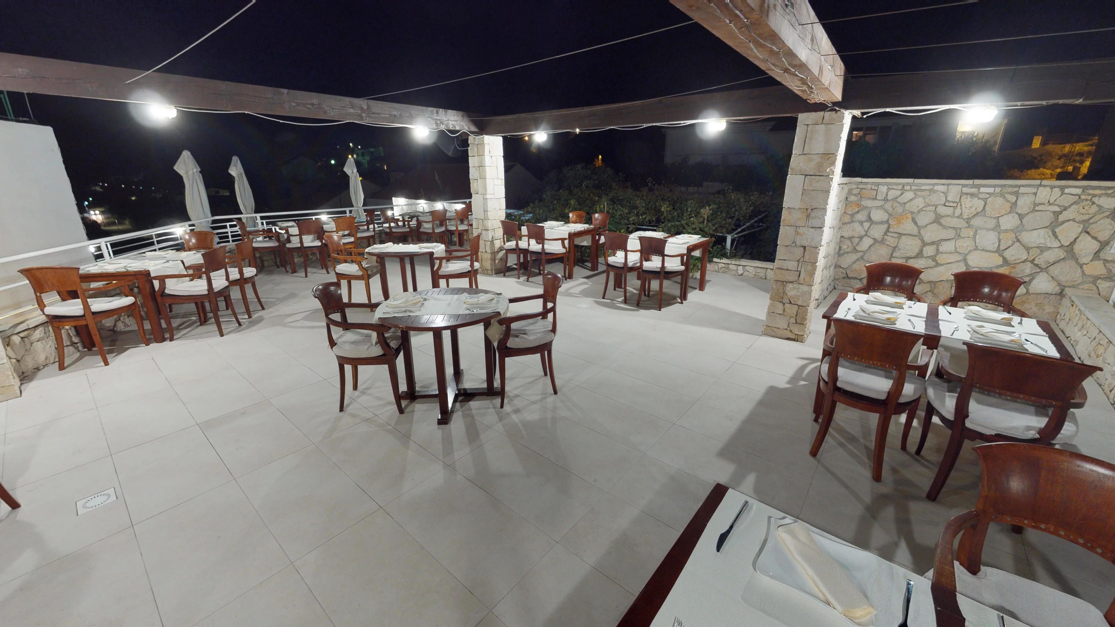 An outdoor patio area with multiple tables and chairs, stone walls, and string lights.