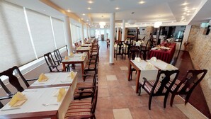 A restaurant with multiple dining tables and chairs, arranged in a spacious layout with a high ceiling and natural light from large windows. - Hotel Belveder (Pag)