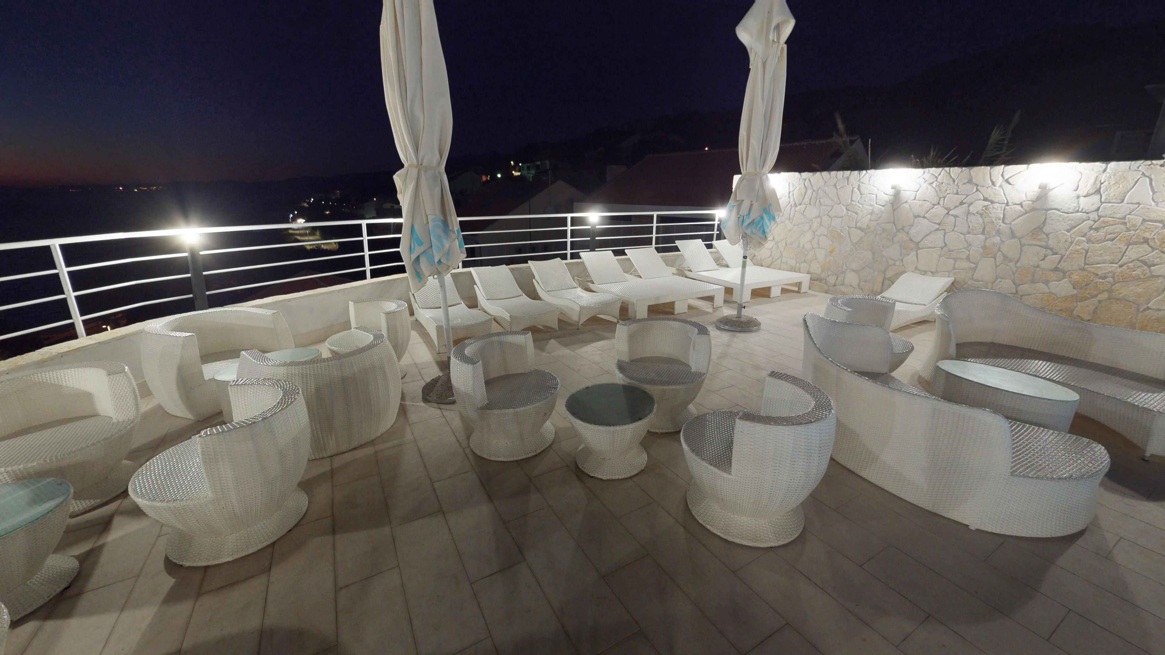 Eine Dachterrasse mit weißen Korbmöbeln, darunter Sofas, Stühle und Tische, sowie eine Steinmauer.