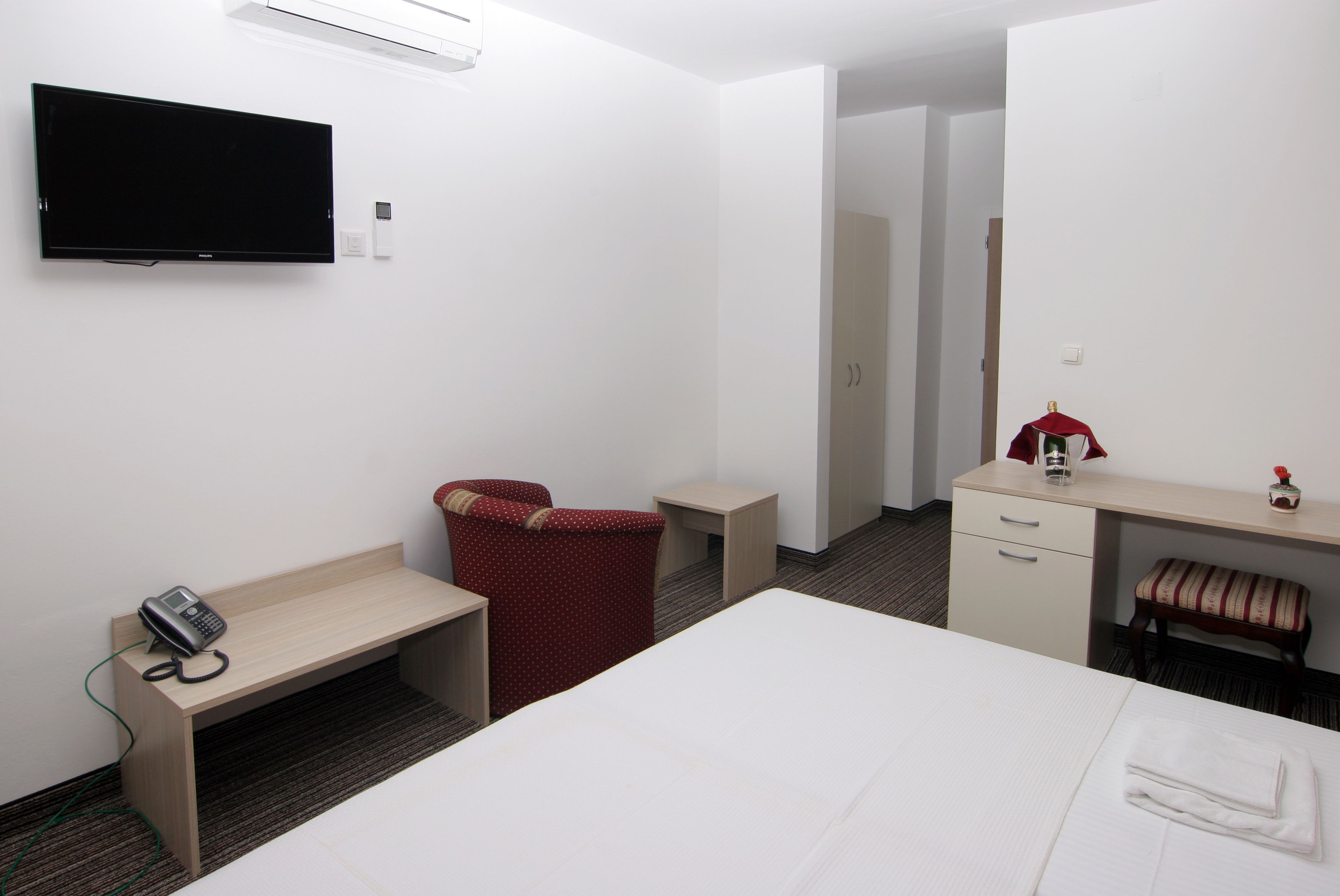 A hotel room with a bed, a desk, a chair, a TV, and a telephone.