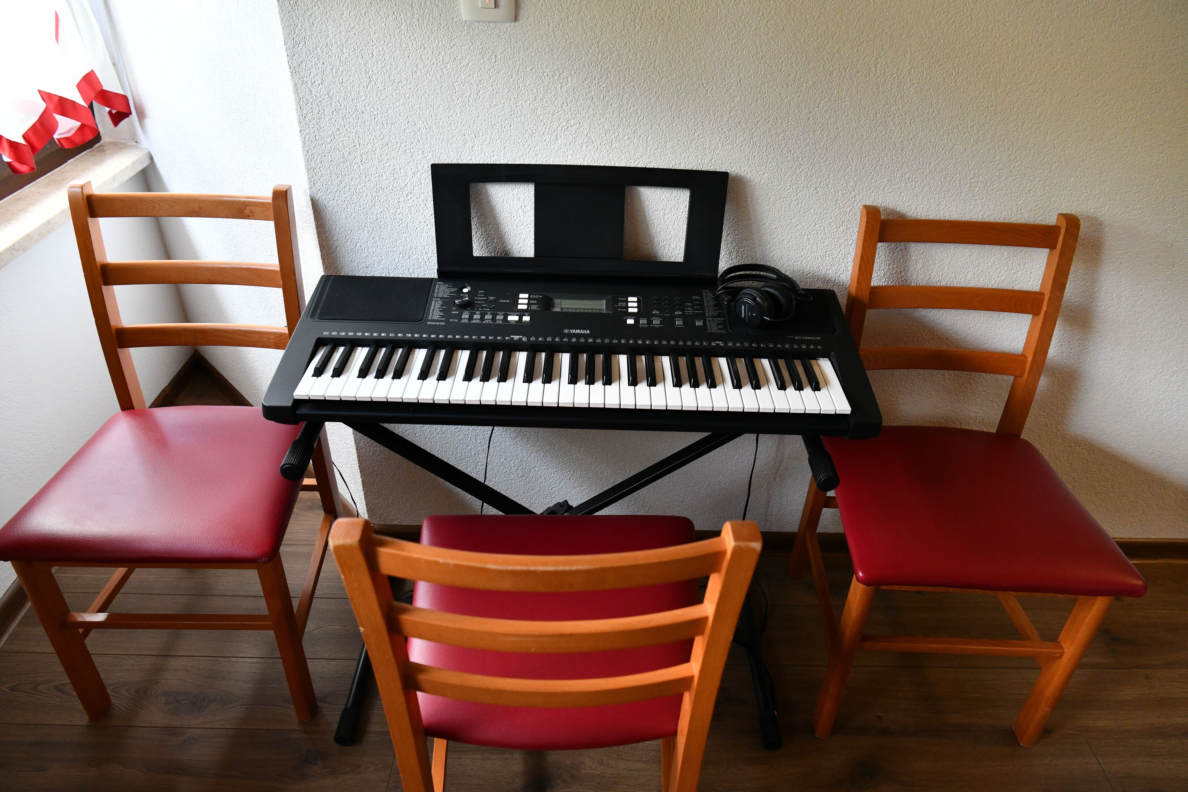 Un clavier Yamaha est posé sur une table, devant laquelle se trouvent deux chaises en bois, l’une avec un siège rouge et l’autre avec un dossier rouge.