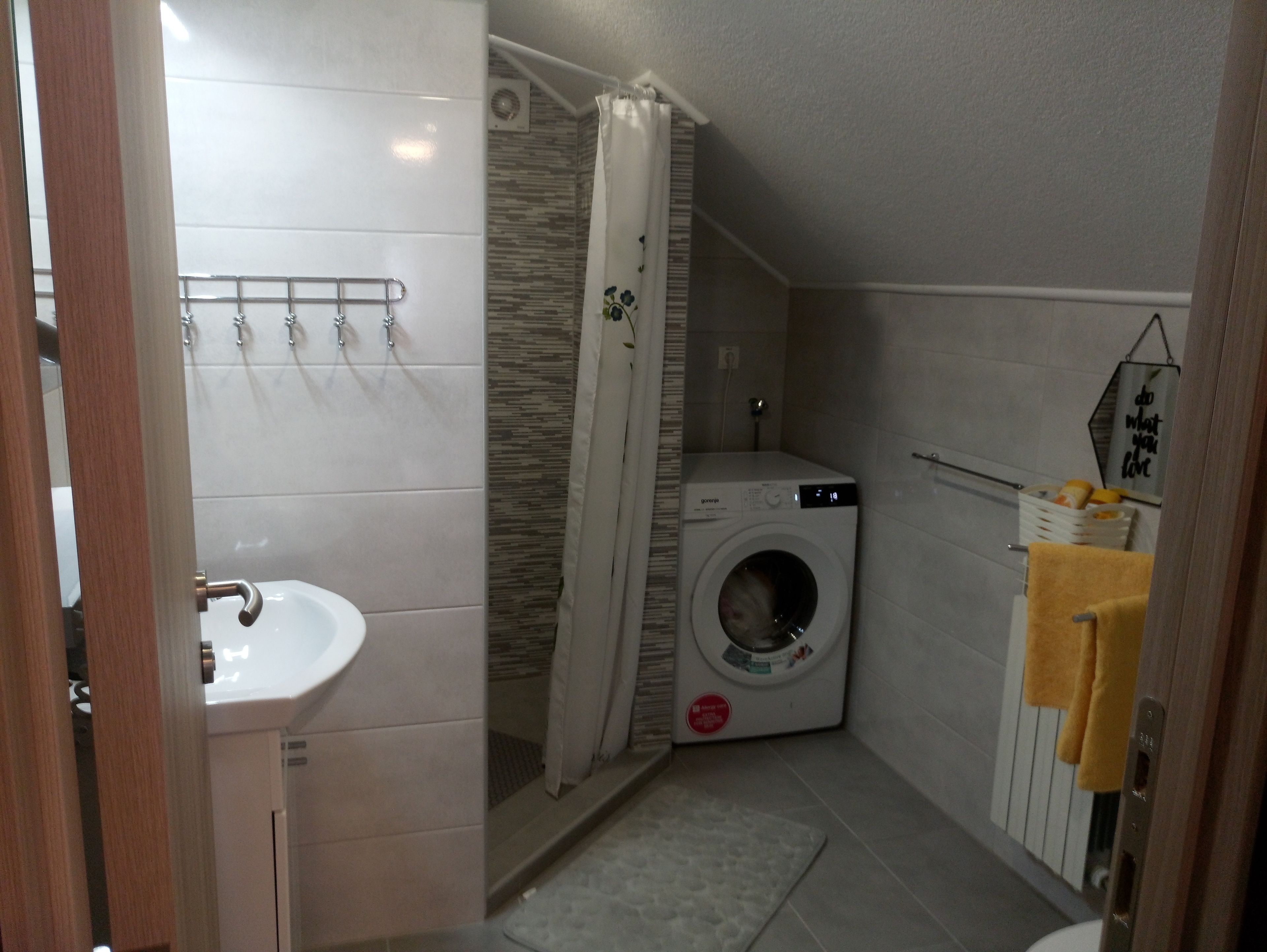 A compact bathroom with a sink, a shower, and a washing machine.
