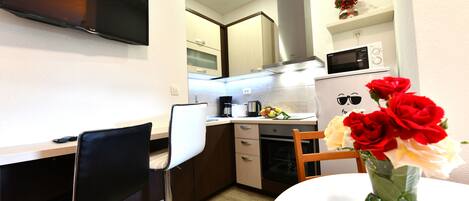 Una cocina moderna con televisor de pantalla plana, microondas y horno. Hay una zona de comedor con mesa y sillas.