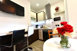 A modern kitchen with a flat-screen TV, microwave, and oven. There is a dining area with a table and chairs.