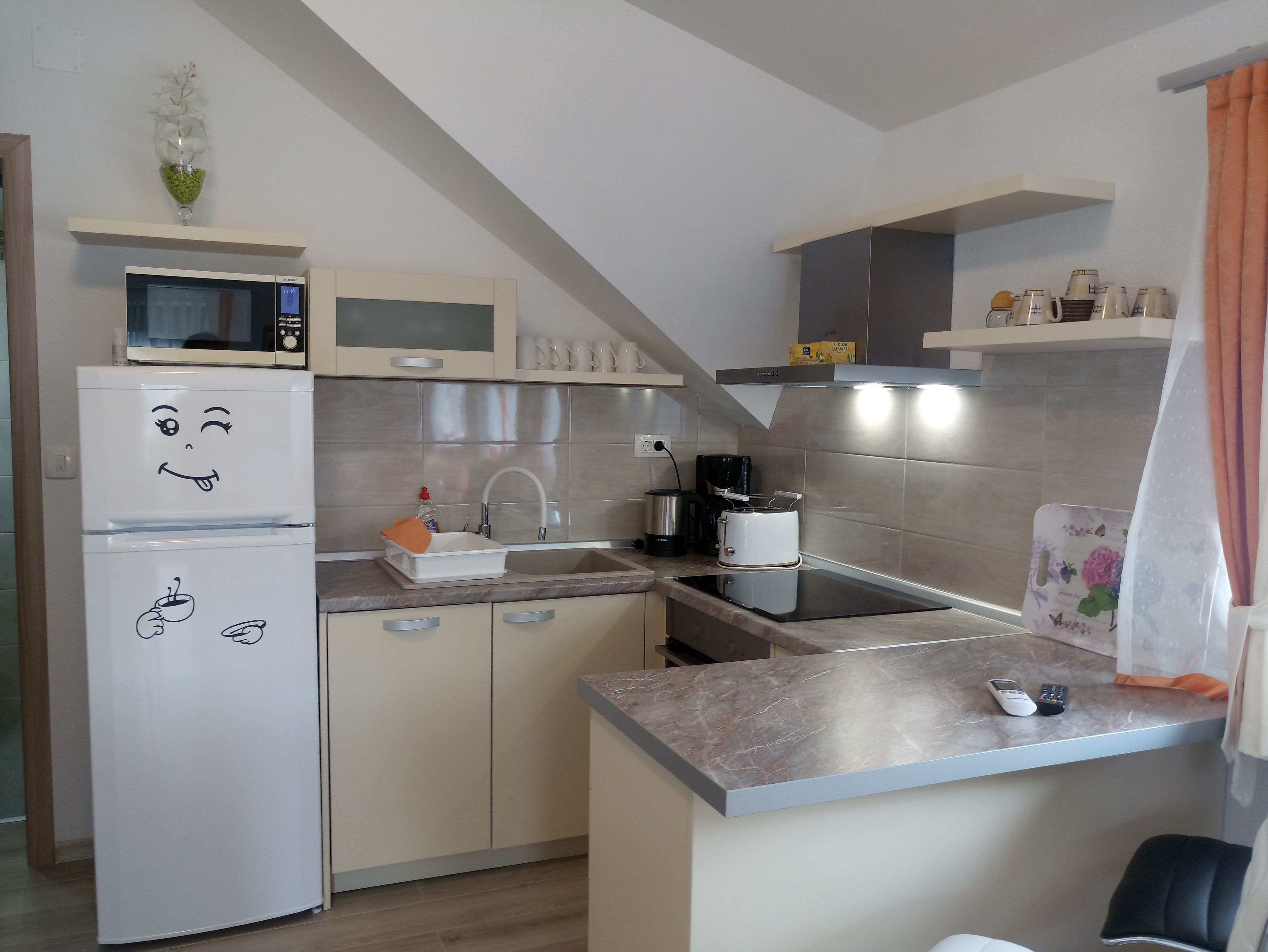 A modern kitchen with a microwave, coffee maker, and a refrigerator with a smiling face design.