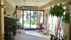 A hotel lobby with a stone fireplace, potted plants, and a view of the outdoor area through large glass doors. - Club Hotel Martin (Bansko)