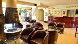A lobby with leather chairs, a stone fireplace, a reception desk, and a clock on the wall. - Club Hotel Martin (Bansko)