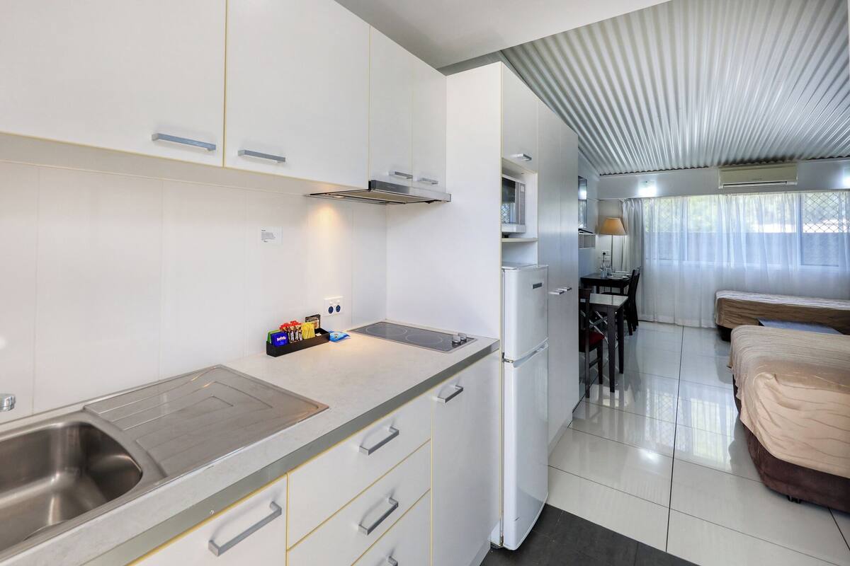 Une cuisine compacte équipée d’un évier, d’une cuisinière et d’un réfrigérateur. Un petit coin repas avec une table et des chaises est également disponible.