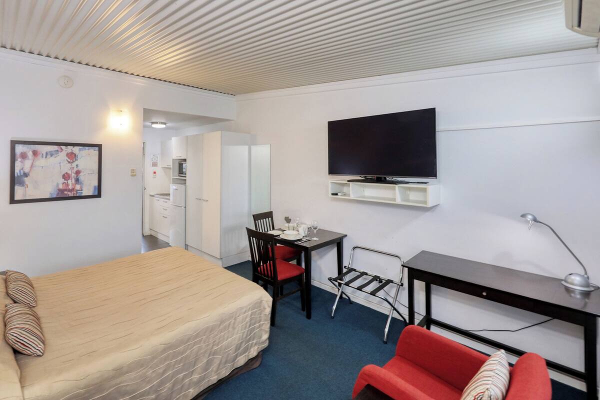 Une chambre d’hôtel équipée d’un lit, d’un bureau, d’une chaise, d’une télévision et d’une petite kitchenette.