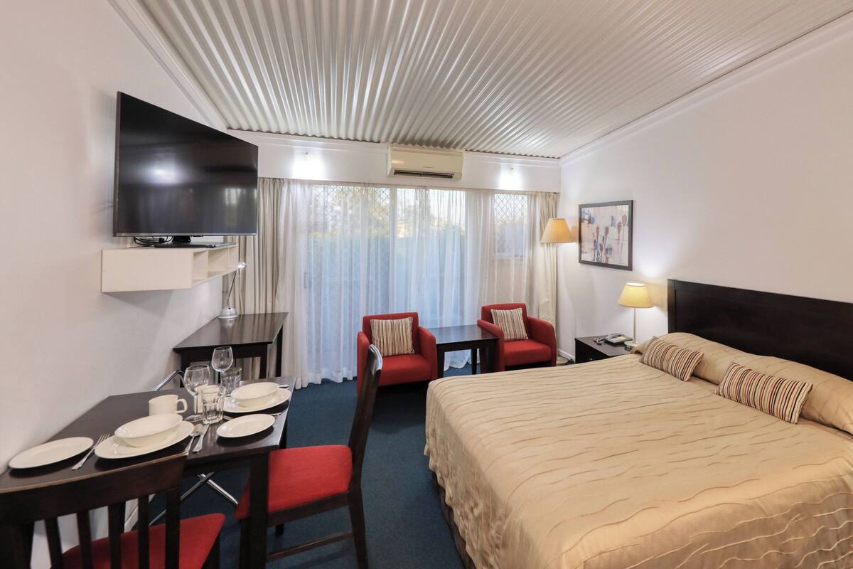 Une chambre d’hôtel comprenant un lit, un bureau avec des chaises, une télévision et une fenêtre avec des rideaux.