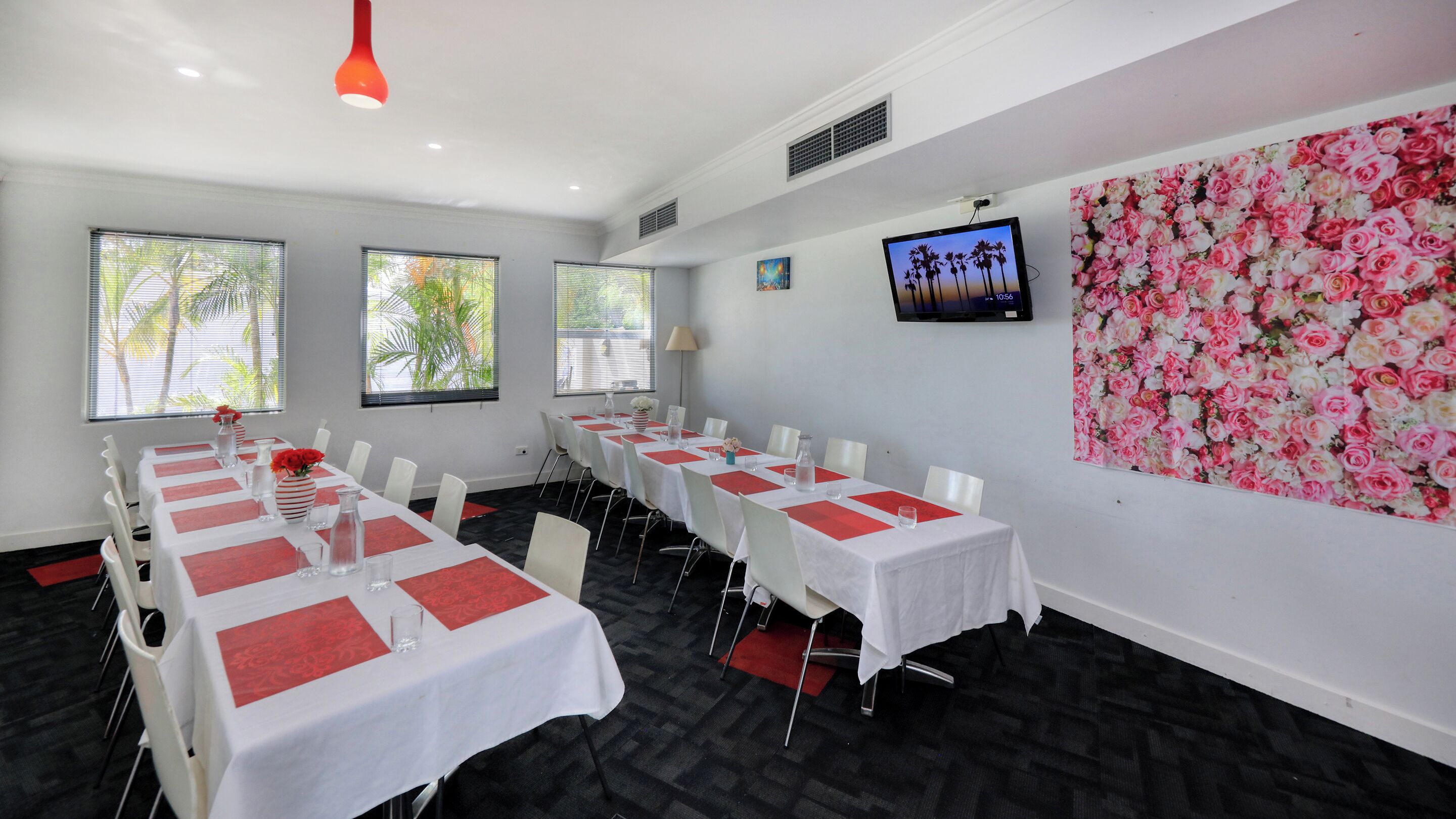 Un salón de conferencias con mesas blancas, detalles en rojo y un mural floral.