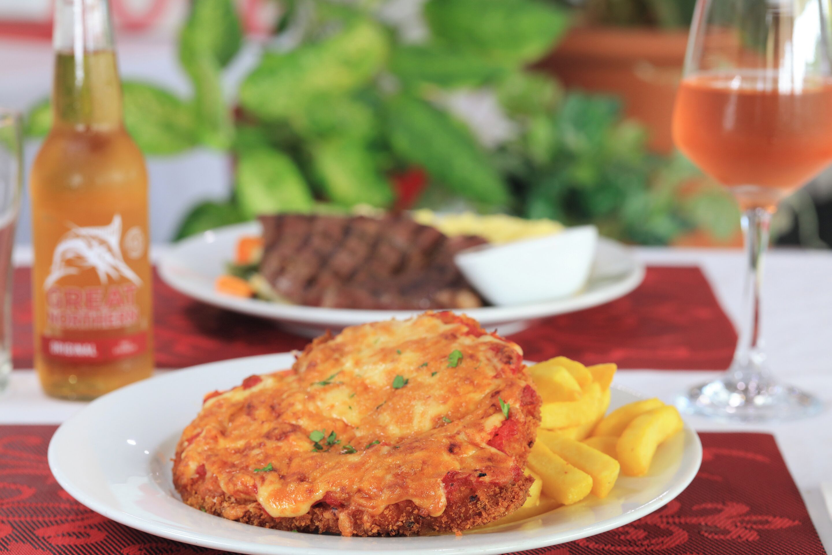A plate of food with a golden-brown crust, a glass of red beverage, and a bottle in the background.