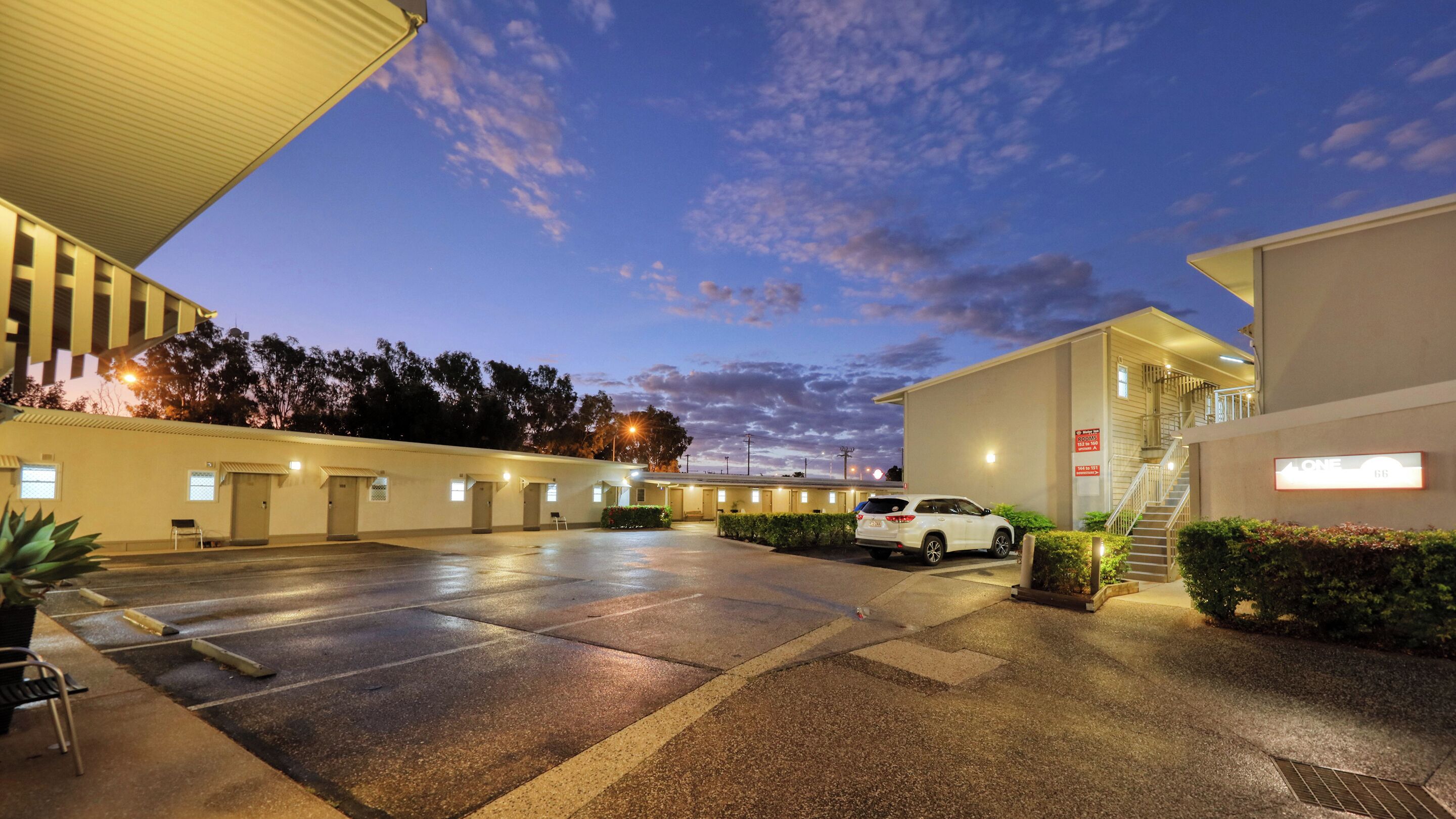 A motel with a parking lot, a white car parked in front, and a staircase leading to the entrance.