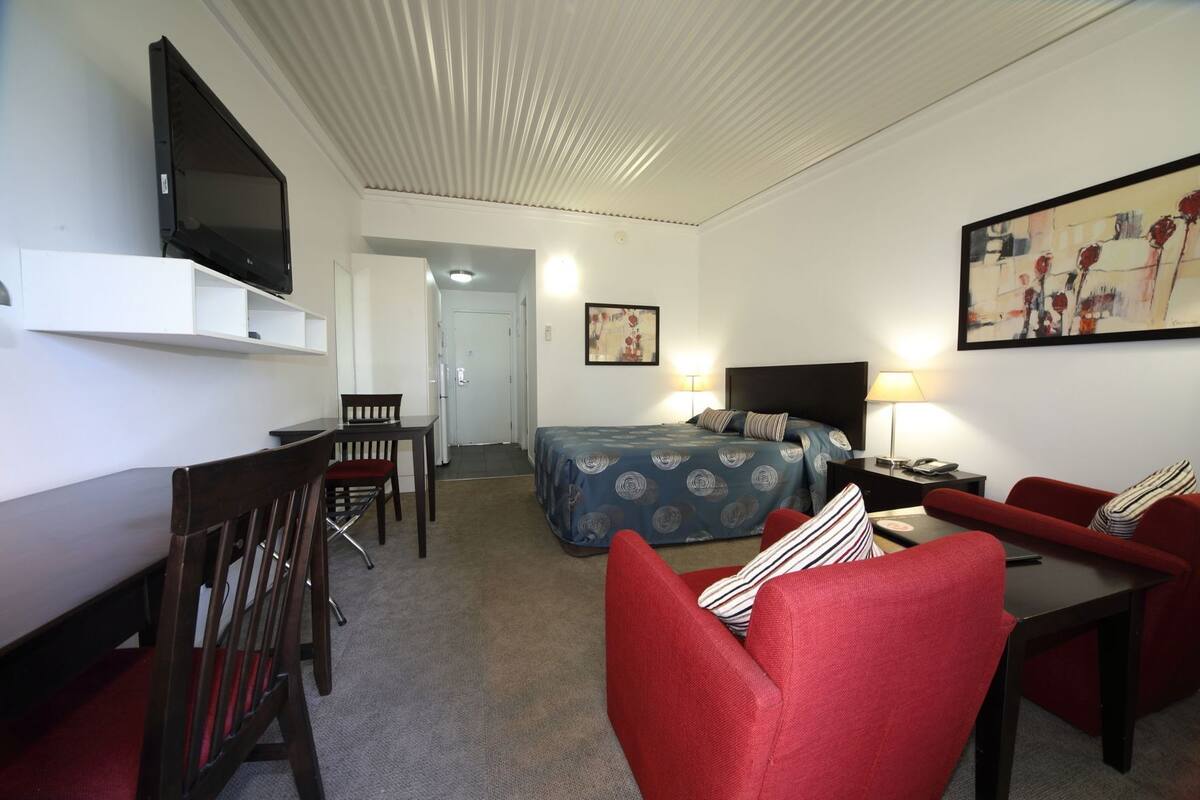 Une chambre d’hôtel avec un lit, un bureau, une chaise, une télévision et un tableau au mur.