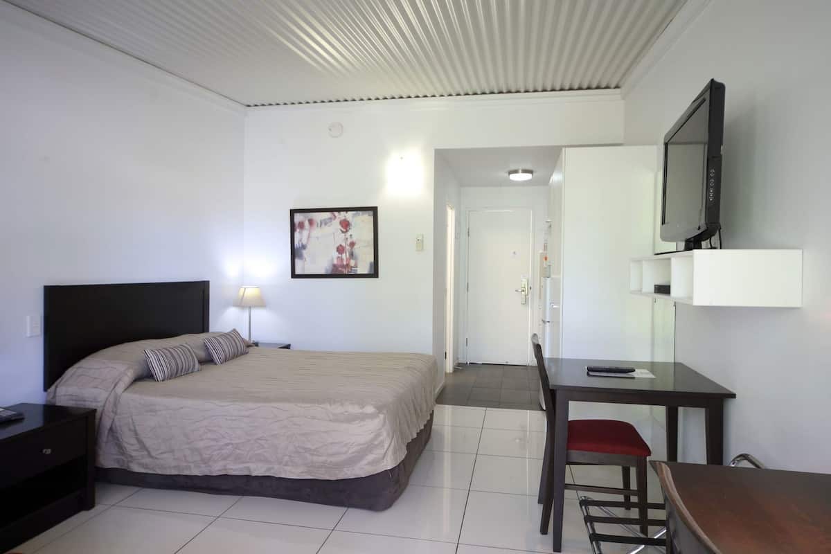 Une chambre d’hôtel comprenant un lit, un bureau, une chaise, une télévision et une porte donnant sur une autre pièce.