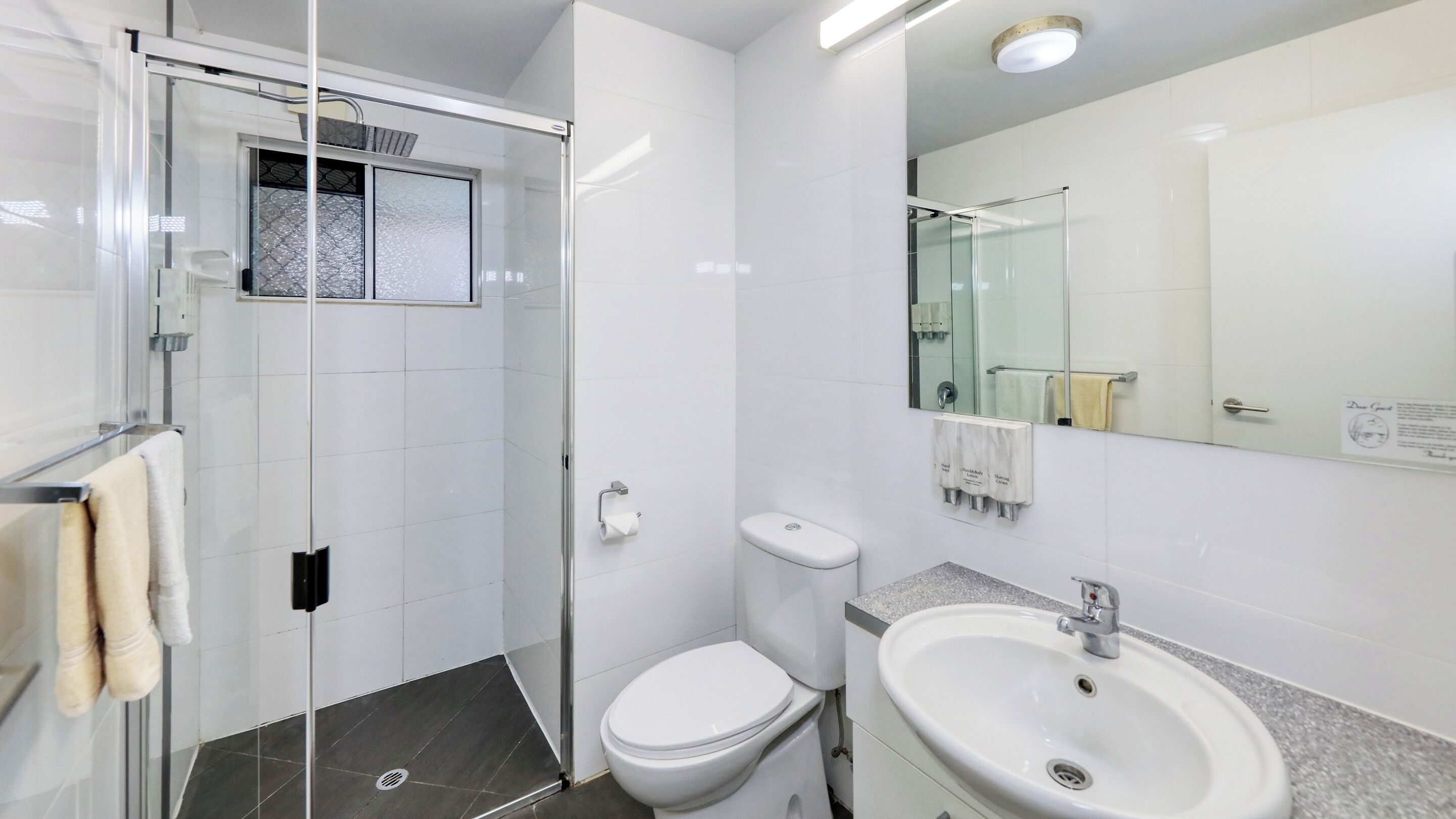 Un bany modern amb un envà de dutxa de vidre, un vàter, un lavabo i un mirall gran.
