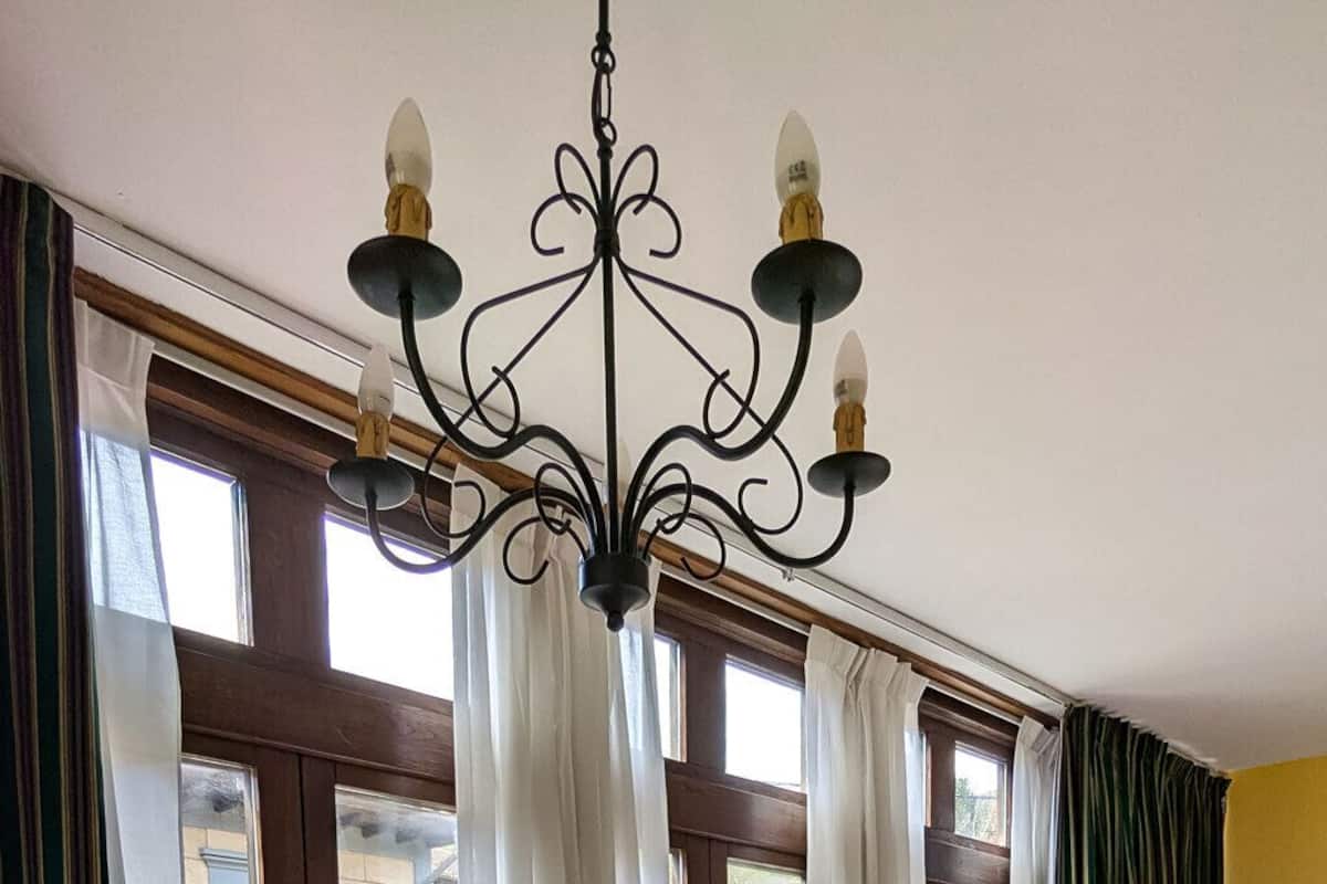 A room with a wooden table, a television, a wooden chair, a chandelier, and large windows with curtains.