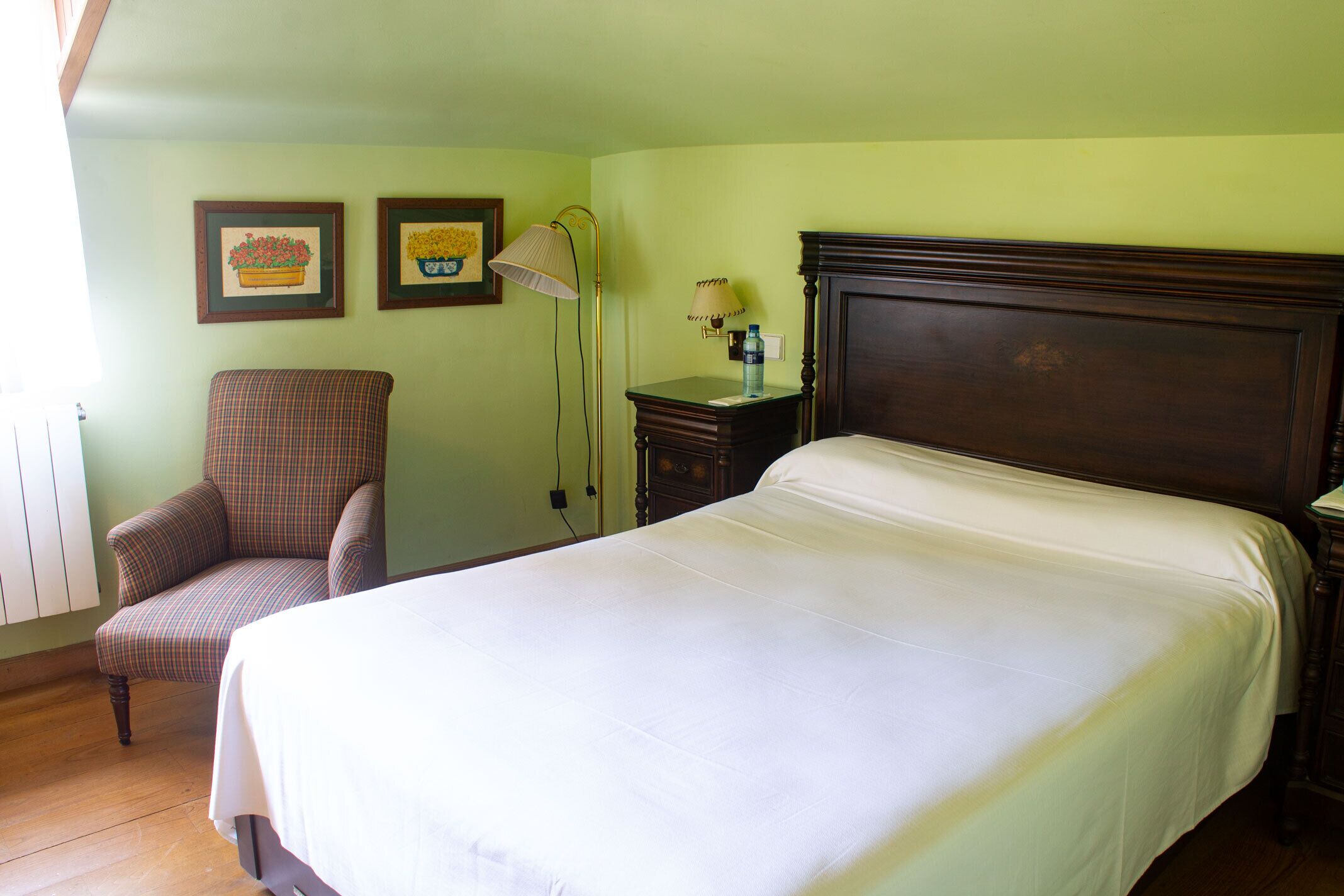 A neatly arranged bedroom with a large bed, a chair, two wall-mounted lamps, and framed pictures on the wall.