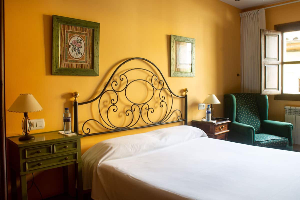 A hotel room with a bed, a nightstand, a lamp, a chair, and two framed pictures on the wall.