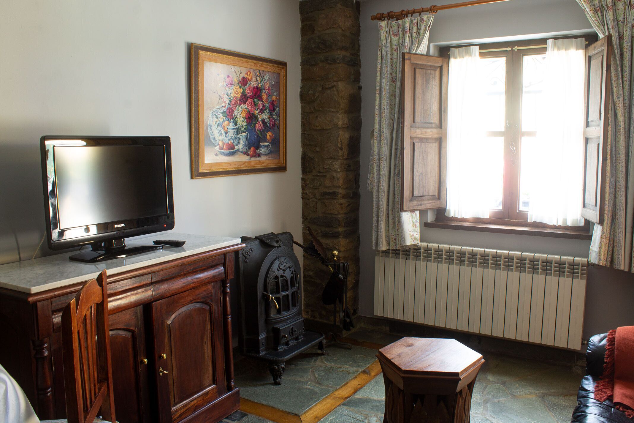 A living room with a television on a wooden cabinet, a stone wall, a fireplace, a window with curtains, and a painting on the wall.