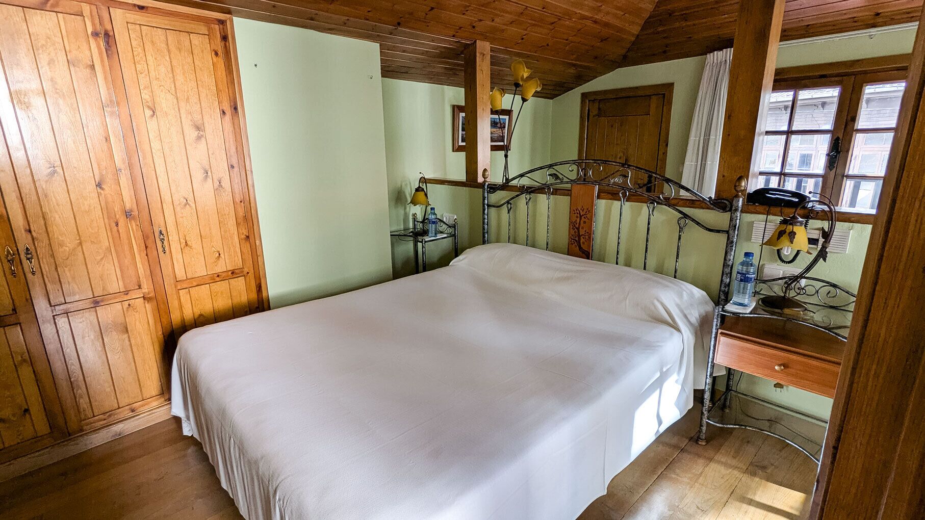 A bedroom with a bed, wooden wardrobe, and a desk with a lamp.