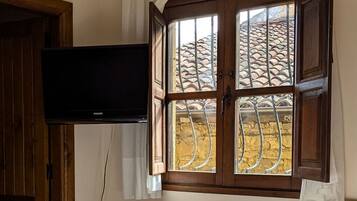 Une pièce comprenant un lit, un bureau en bois, une chaise, un téléviseur fixé au mur et une fenêtre donnant sur un toit recouvert de tuiles.