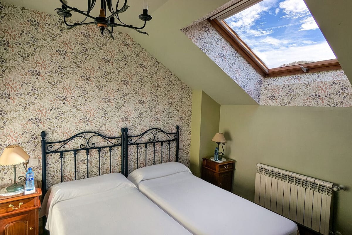 A bedroom with a bed, a nightstand, a lamp, a radiator, and a skylight.