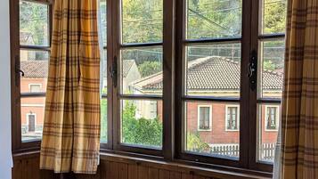 A room with wooden walls, a window with curtains, a radiator, and a bed with a checkered blanket.