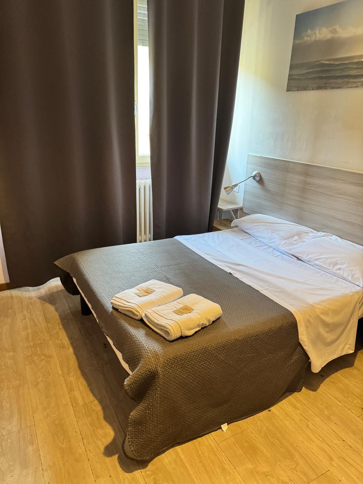 Una camera d'albergo con un letto, una lampada da comodino e vista sull'esterno.