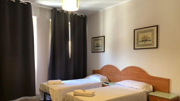 Habitación de hotel con dos camas individuales, cabecero de madera, mesita de noche y un cuadro enmarcado en la pared.