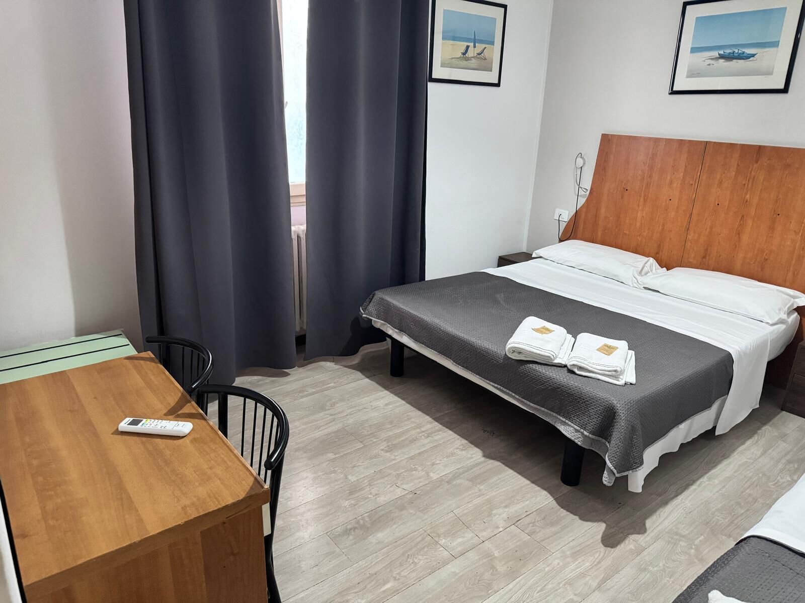 A hotel room with a bed, a wooden desk, a chair, and a remote control on the desk.