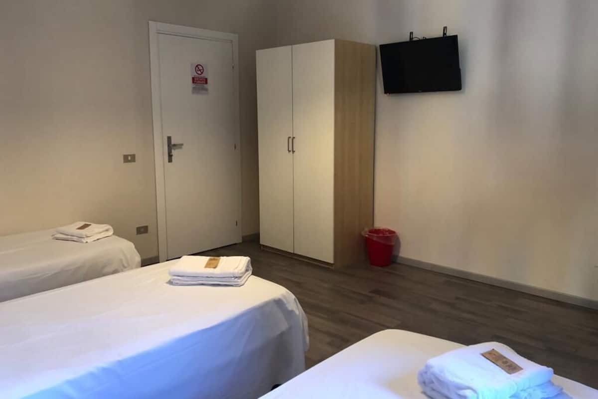 A hotel room with two beds, a wardrobe, a television, and a red trash bin.