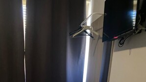 Una habitación con un banco de madera, un espejo, un televisor montado en la pared y una ventana con cortinas.