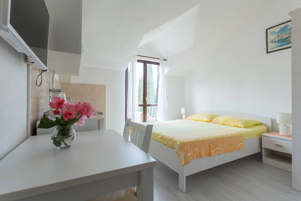 A bedroom with a bed, bedside table, and a small table with a vase of flowers.