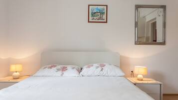 Een slaapkamer met een bed, twee nachtkastjes met lampen, een lijst met een schilderij en een spiegel aan de muur.