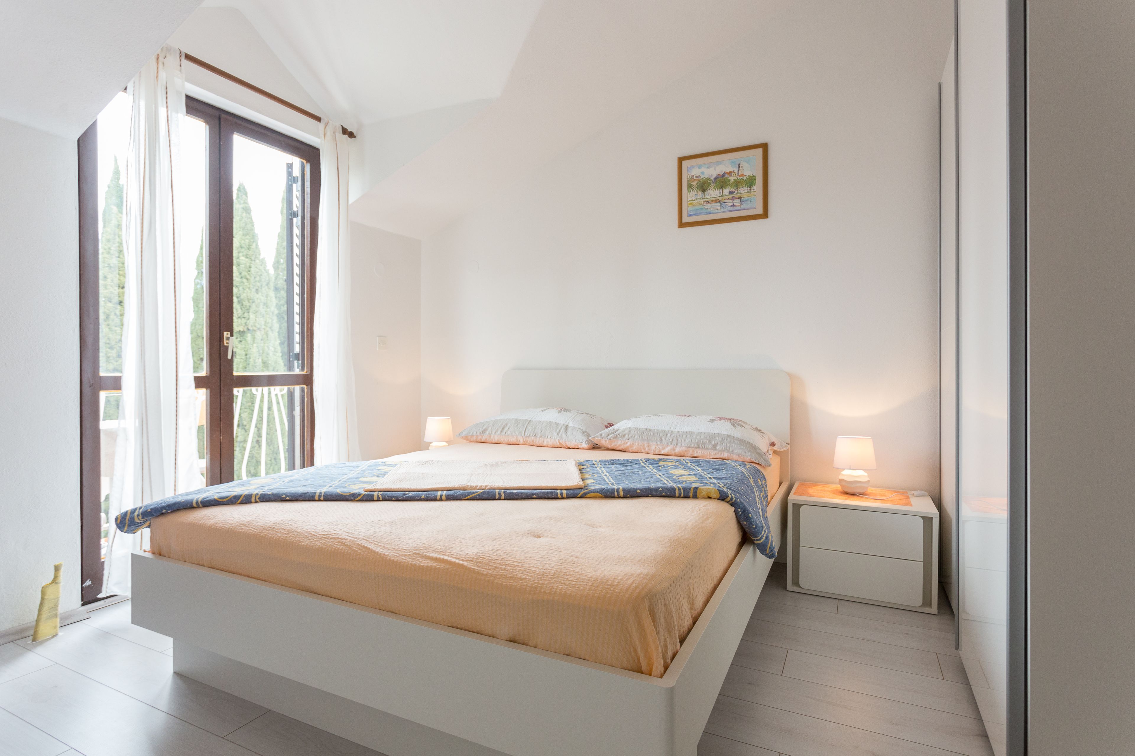 A bedroom with a bed, nightstands, a window with curtains, and a wall-mounted picture.