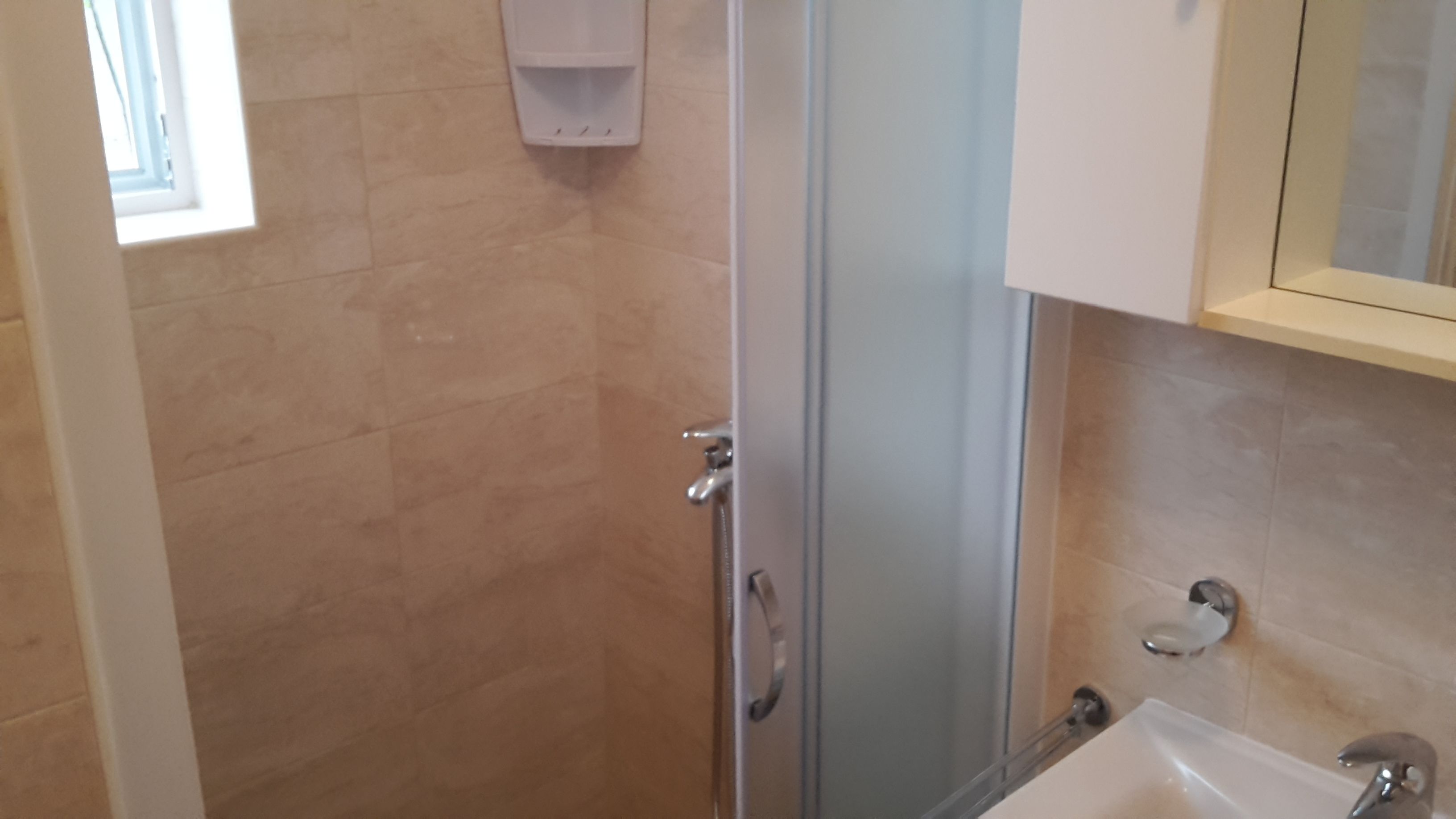 Un baño con cabina de ducha de vidrio, un lavabo blanco y un espejo sobre él.