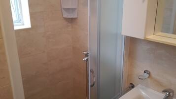 Un baño con cabina de ducha de vidrio, un lavabo blanco y un espejo sobre él.