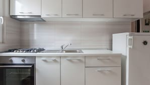 A modern kitchen with white cabinetry, a built-in oven, a stainless steel range hood, and a white refrigerator. - Villa Anka (Konavle)