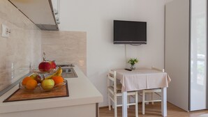 A modern kitchen with a fruit bowl, a table with a vase, and a TV on the wall. - Villa Anka (Konavle)