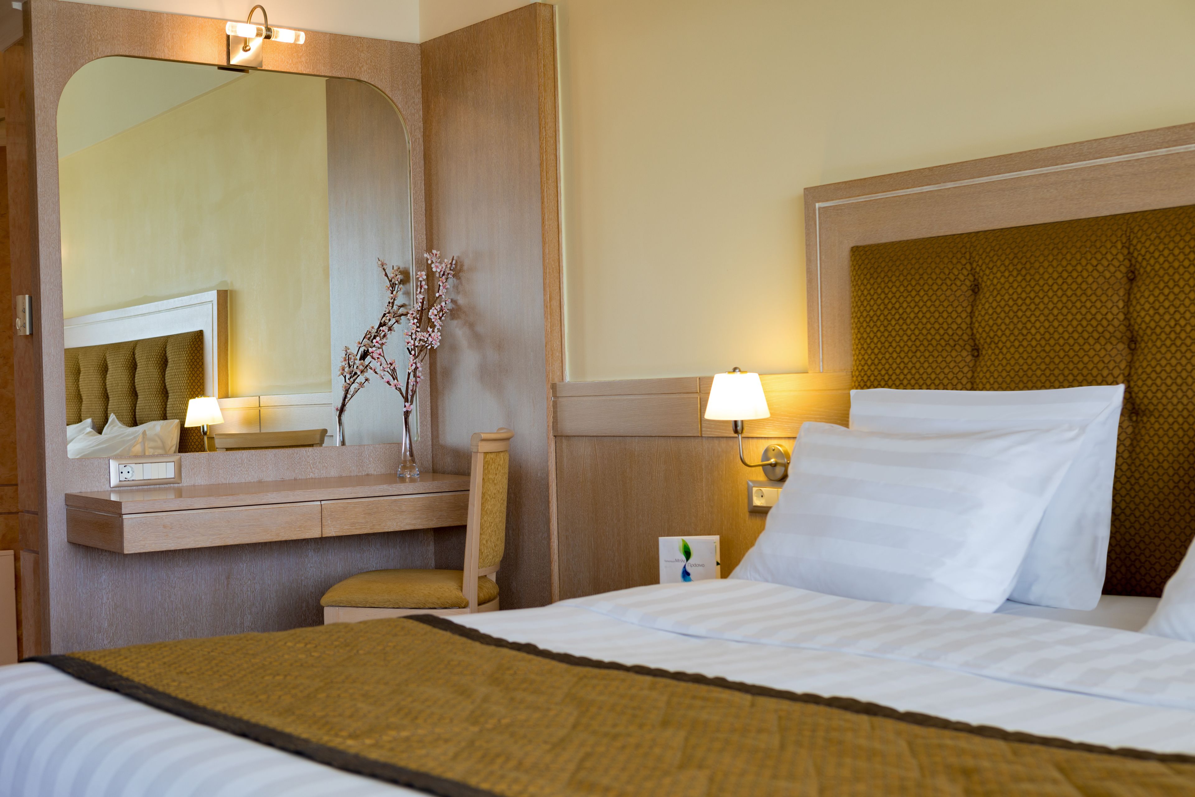 Una habitación de hotel con una cama grande, una mesita de noche, un espejo y una lámpara.