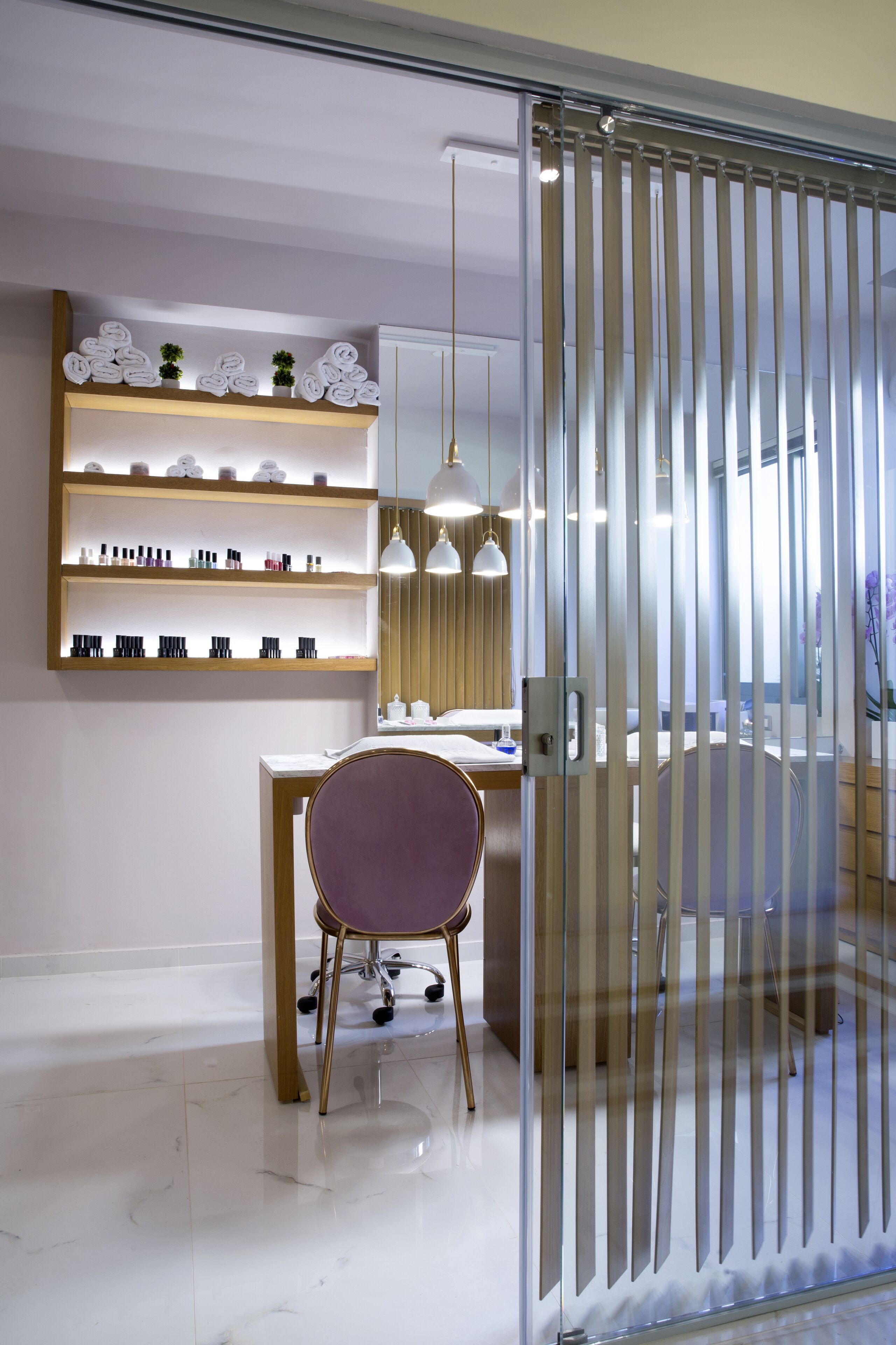 Ein modernes Zimmer mit Glastrennwand, einem Holztisch, einem Stuhl und Regalen mit Pflegeprodukten.