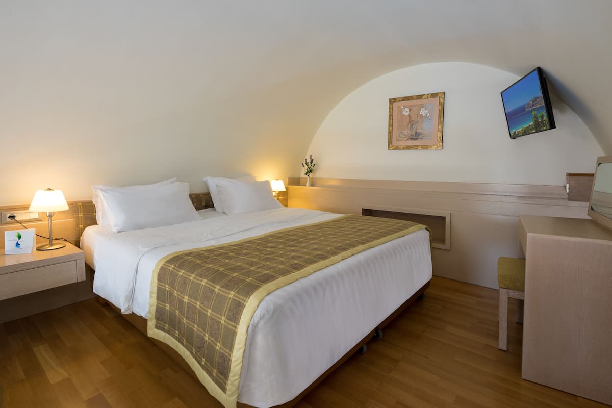 Quarto de hotel com cama, mesas de cabeceira, escrivaninha e televisão.