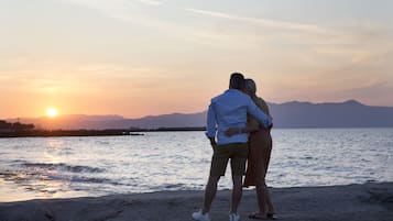 A couple standing by a body of water during sunset with mountains in the background.