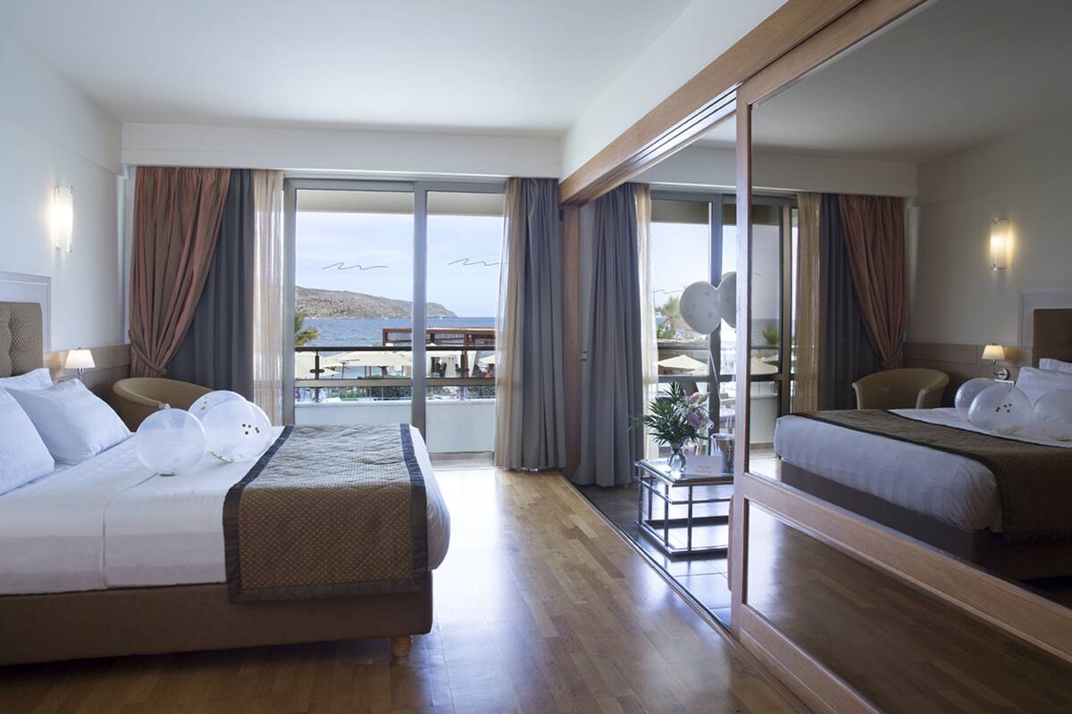 Quarto de hotel com duas camas, varanda e vista para o mar, e um espelho grande.