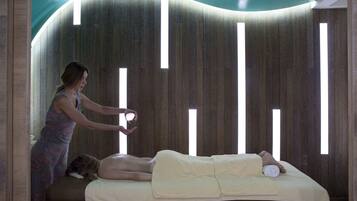 A massage therapy room with a wooden wall, a massage table, and a person performing a massage.